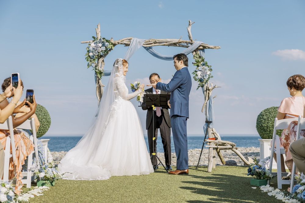 Wedding ceremony site with wooden arch decorated with greenery against an ocean backdrop.
