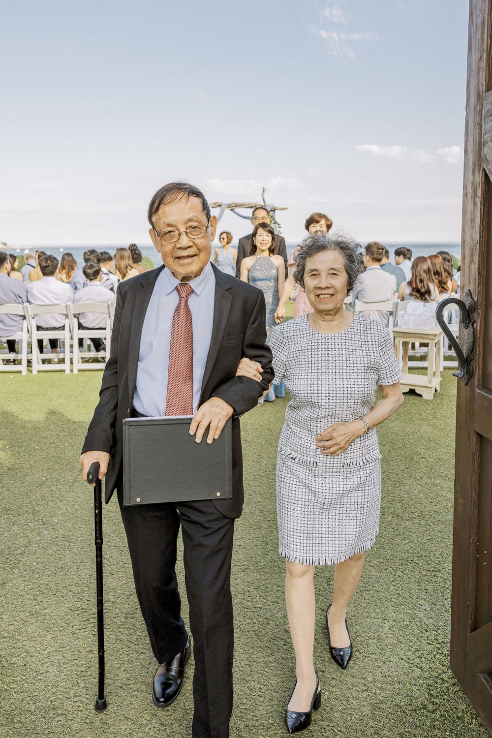 Outdoor wedding celebration on a grassy lawn with white chairs set up for guests.