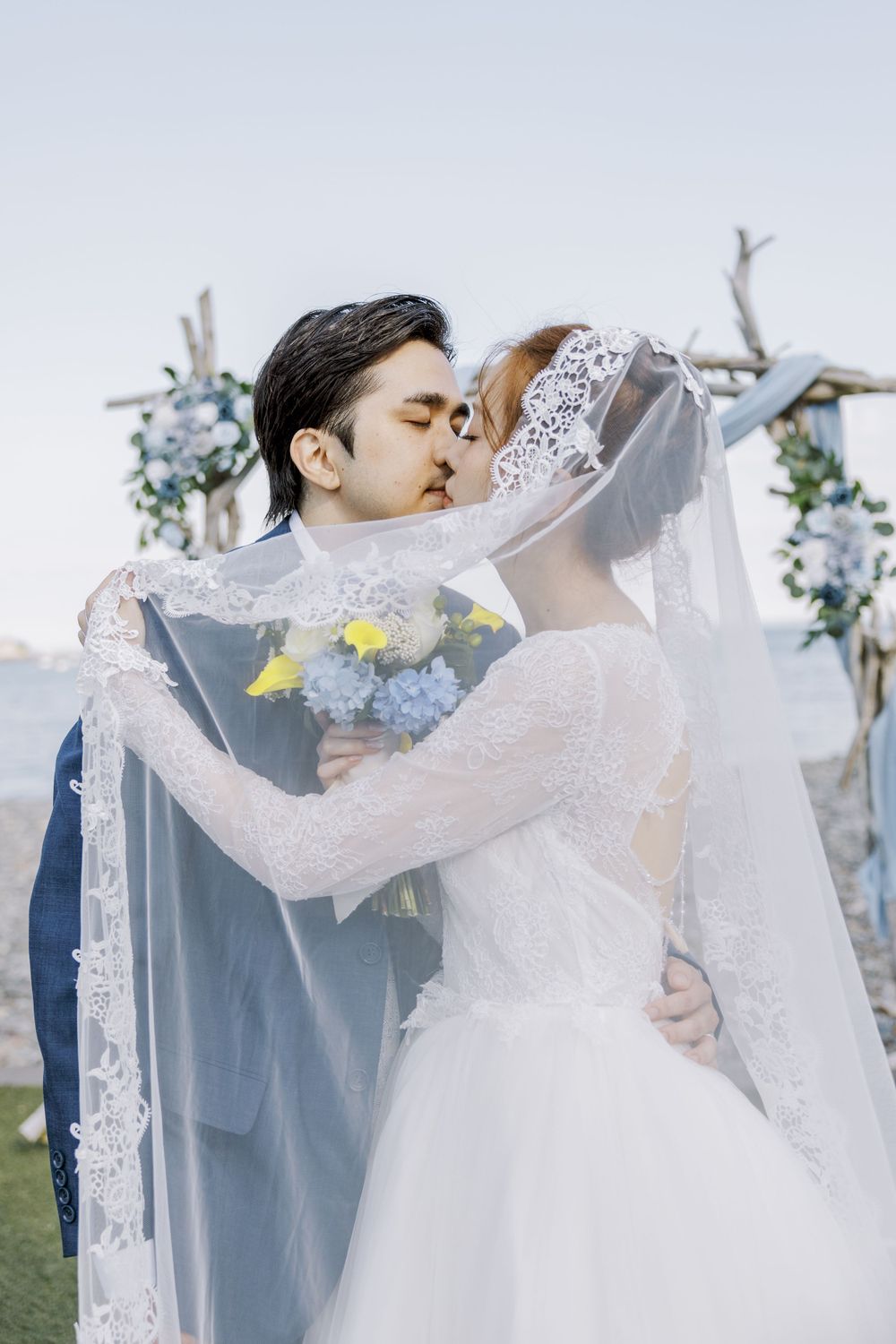 A romantic wedding kiss scene under a floral arch with delicate lace veil details.