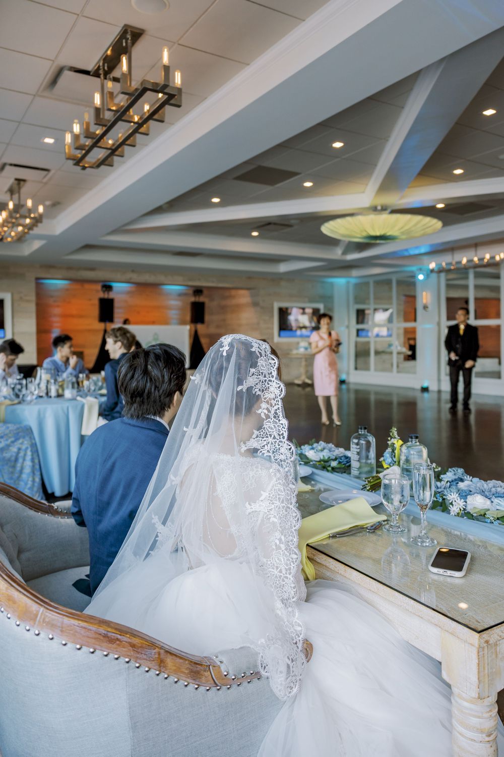 Wedding reception in modern venue with crystal chandeliers and blue-themed table settings.