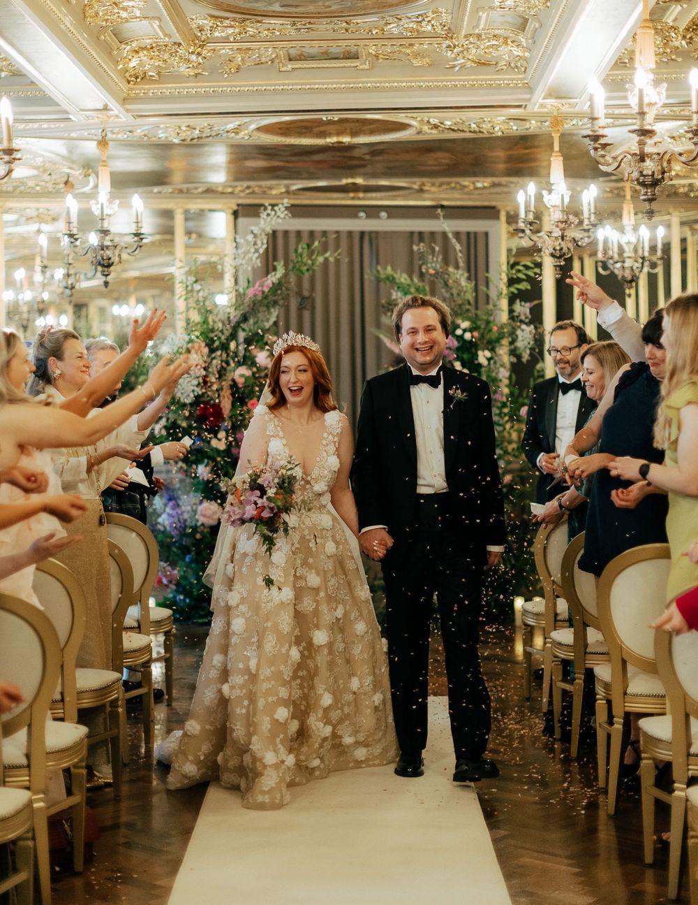 Wedding celebration in an ornate ballroom with guests dancing and celebrating under sparkling chandeliers.