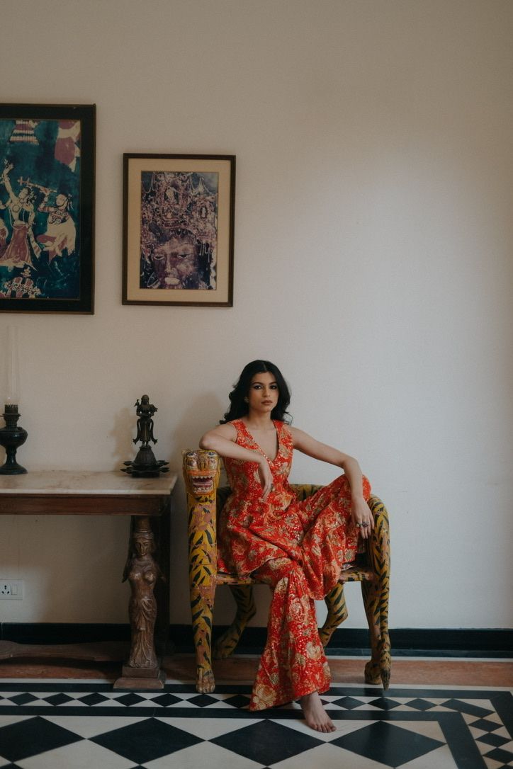 Interior portrait showing red traditional outfit while seated in carved wooden chair.