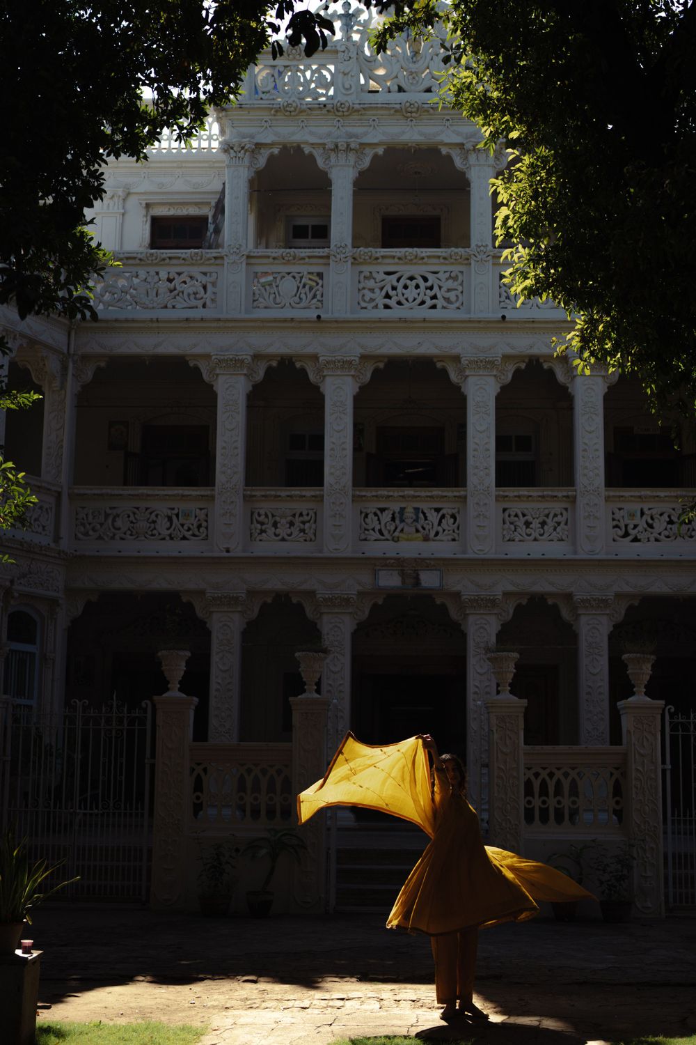Figure in flowing yellow dress twirls in front of ornate white colonial architecture.