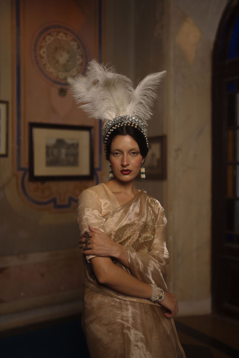 Classic Hollywood glamour portrait with model wearing cream vintage dress and feather accessory in dimly lit setting.
