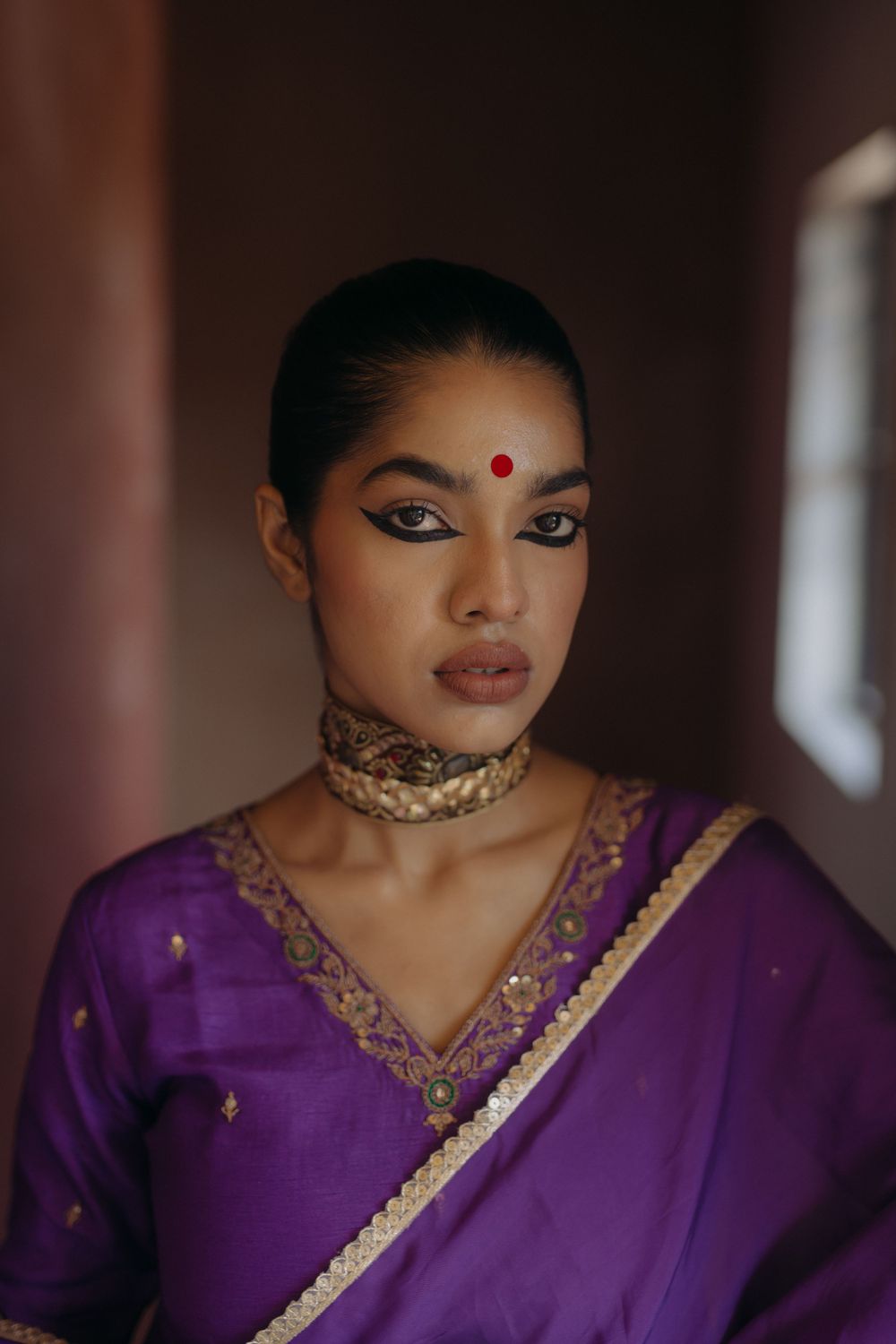 Portrait showcasing traditional South Asian attire with purple sari and intricate gold jewelry.