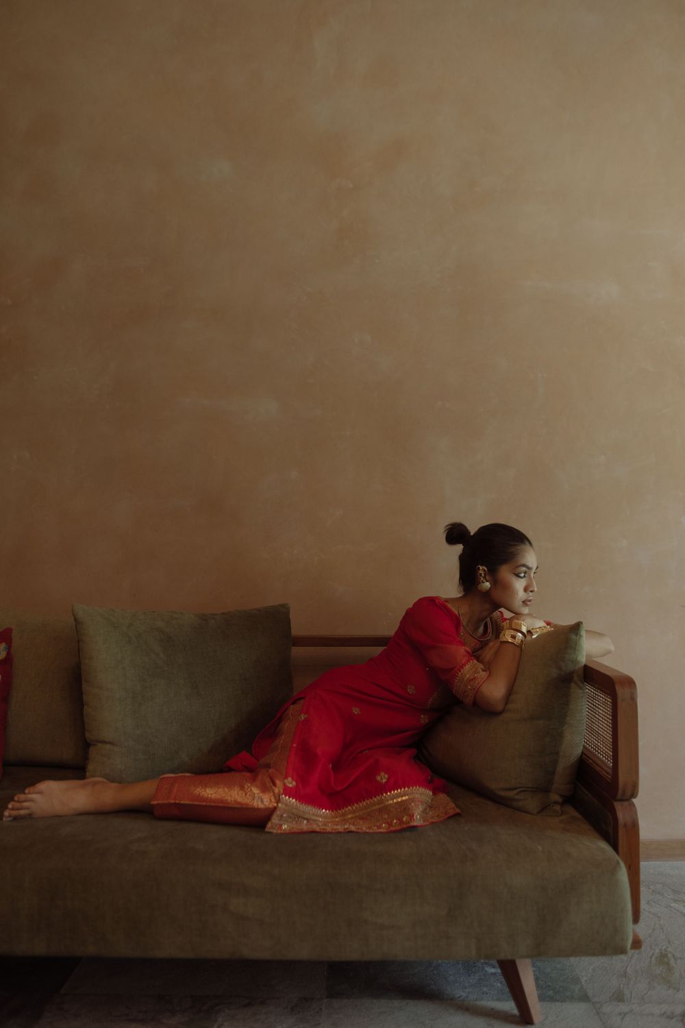Artistic portrait of person in red traditional dress reclining on olive green modern sofa.