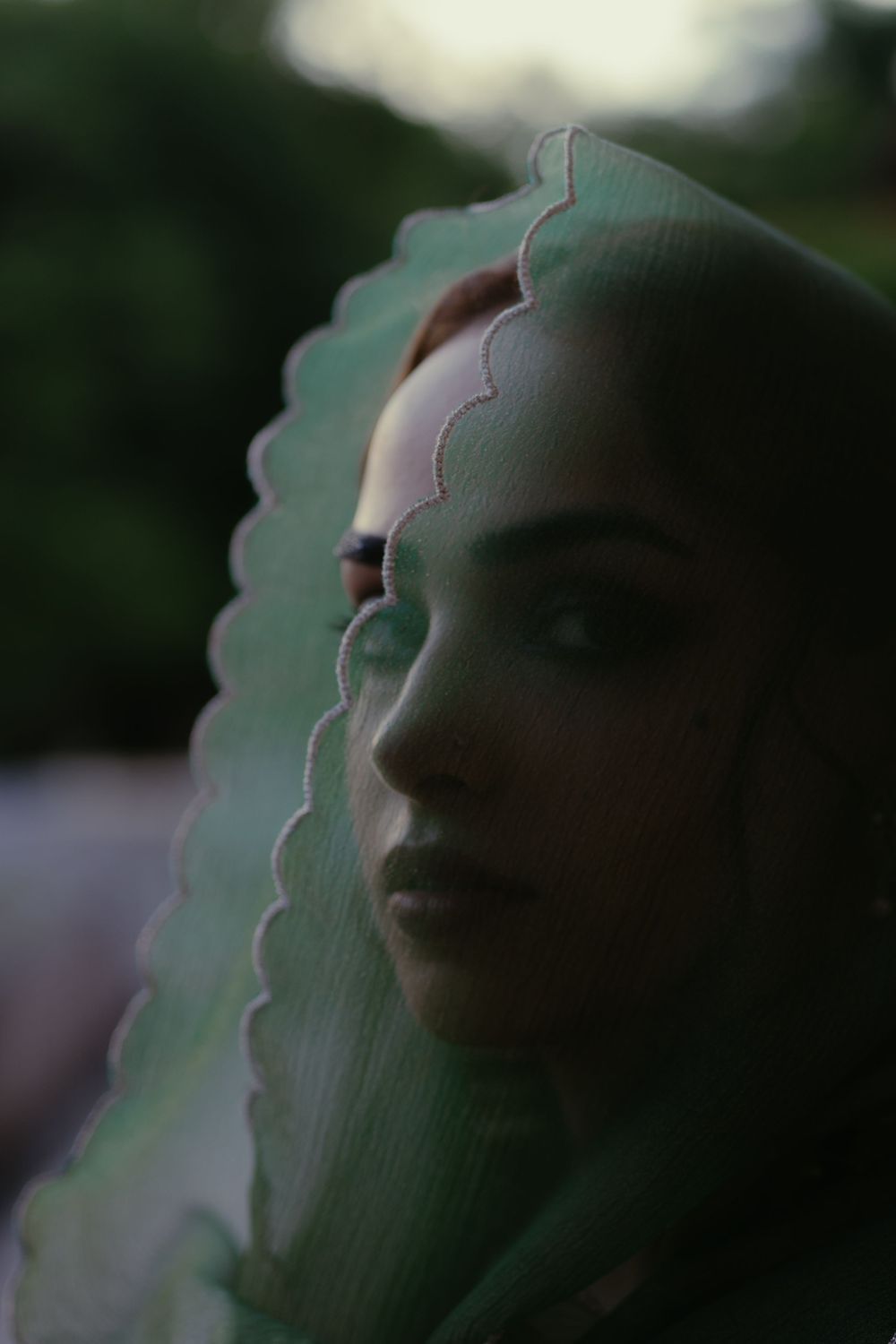 A series of successive facial profile silhouettes against a blurred green natural background creates a haunting visual effect.