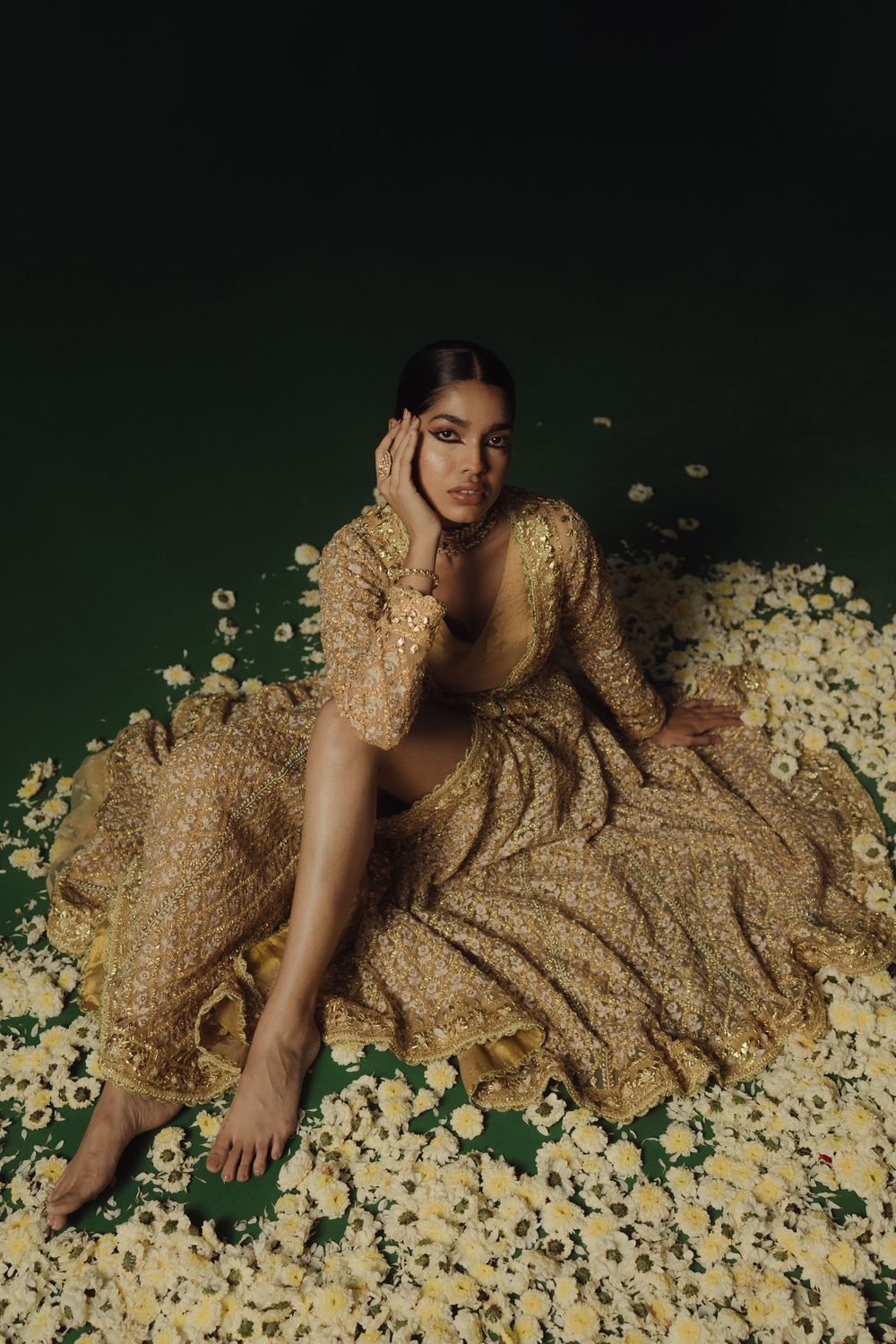 Series of artistic fashion photos showing floral scattered petals and gold fabric against a dark green background.