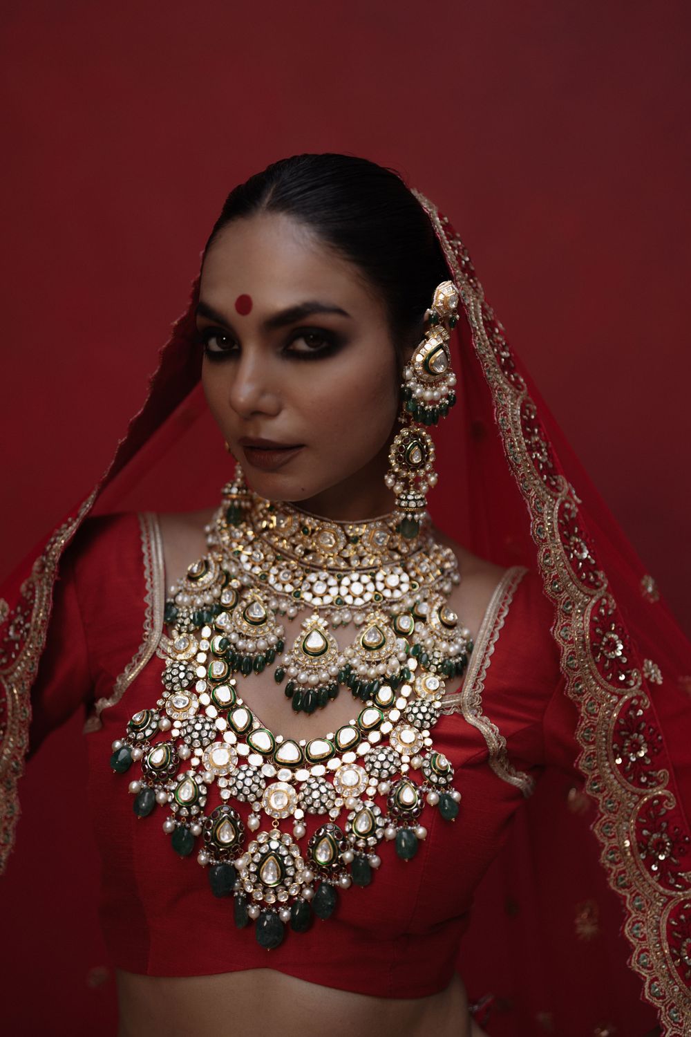 Rich Indian bridal jewelry featuring ornate gold necklaces and earrings against a deep red backdrop.