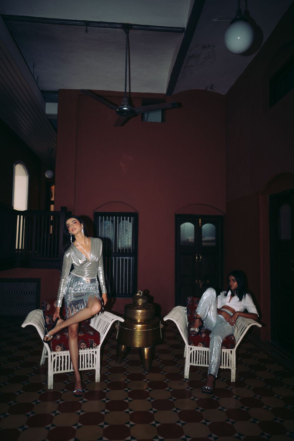 Fashion editorial with models posing on white chairs in moody vintage interior.