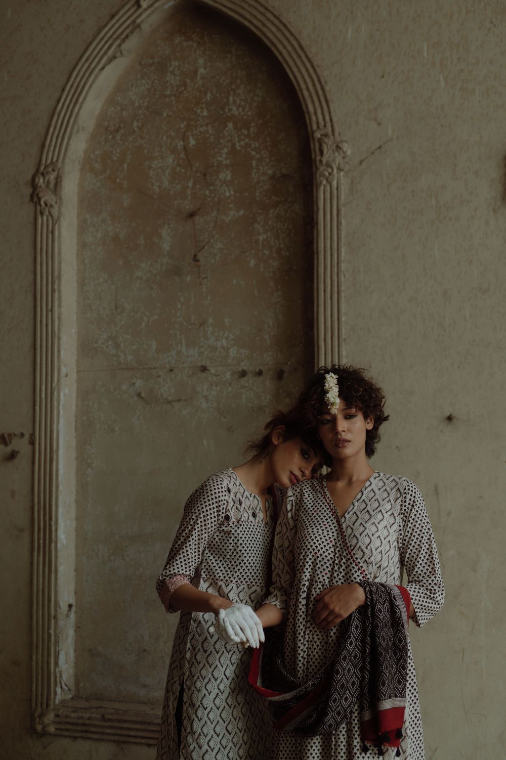 Artistic portrait of two people in matching printed dresses against arched stone doorway.
