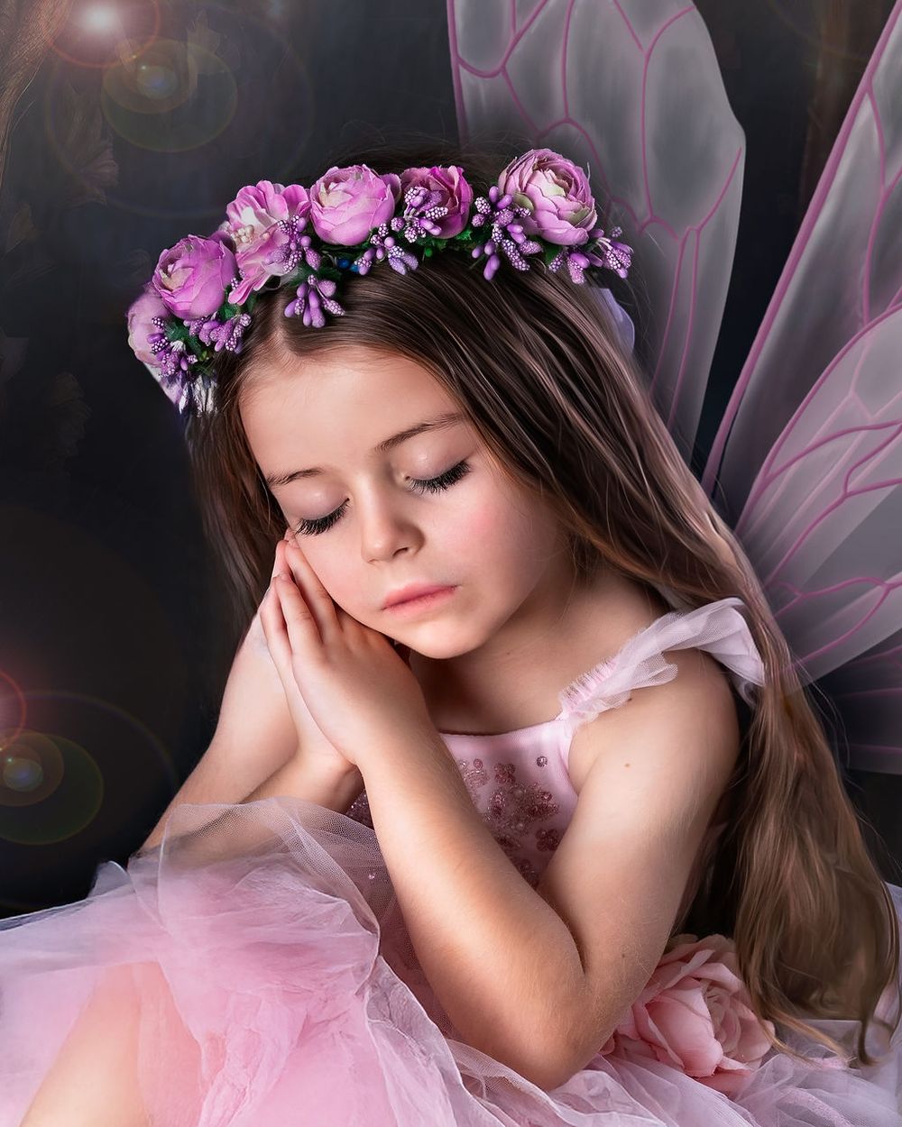 A young girl dressed as a fairy with pink tulle dress, floral crown, and butterfly wings poses dreamily.