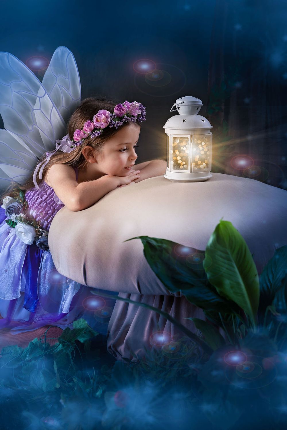 A young girl dressed as a fairy with wings and floral crown gazes at a glowing lantern in a magical night scene.