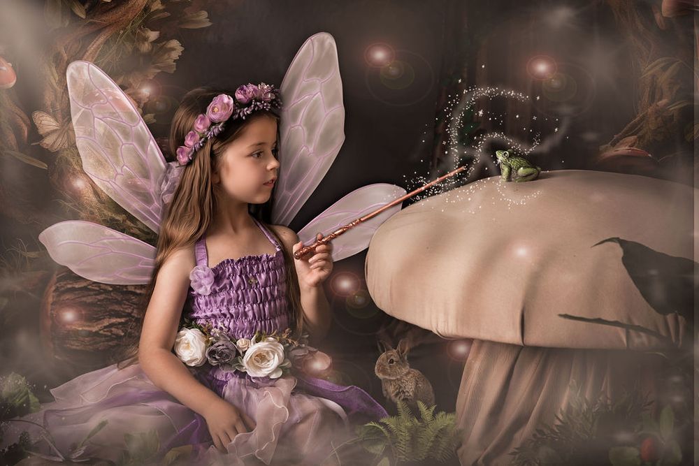 A young girl dressed as a fairy in purple with wings and floral crown touches a magic wand to a glowing mushroom.