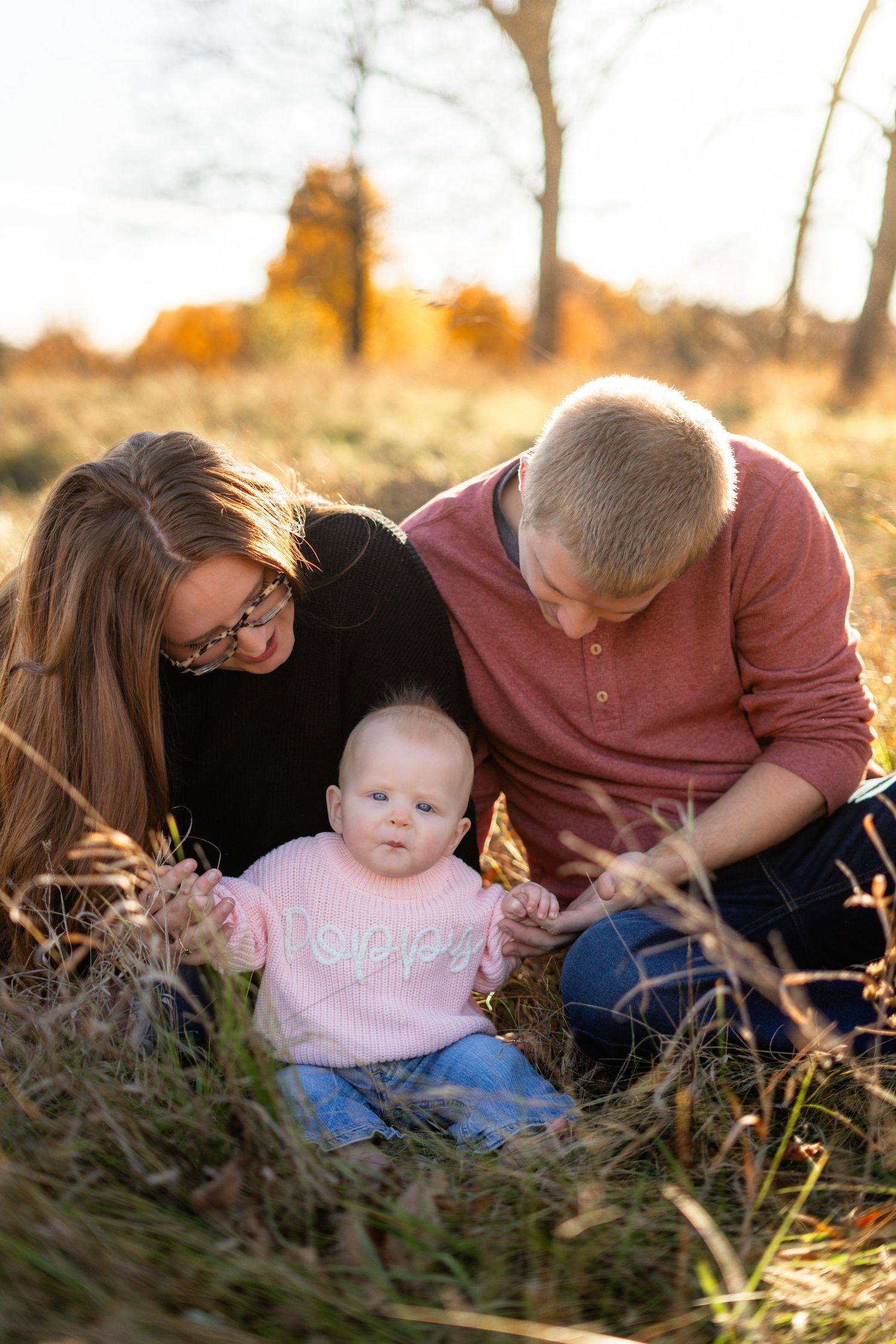 A family with baby sitting together in tall grass during sunset.