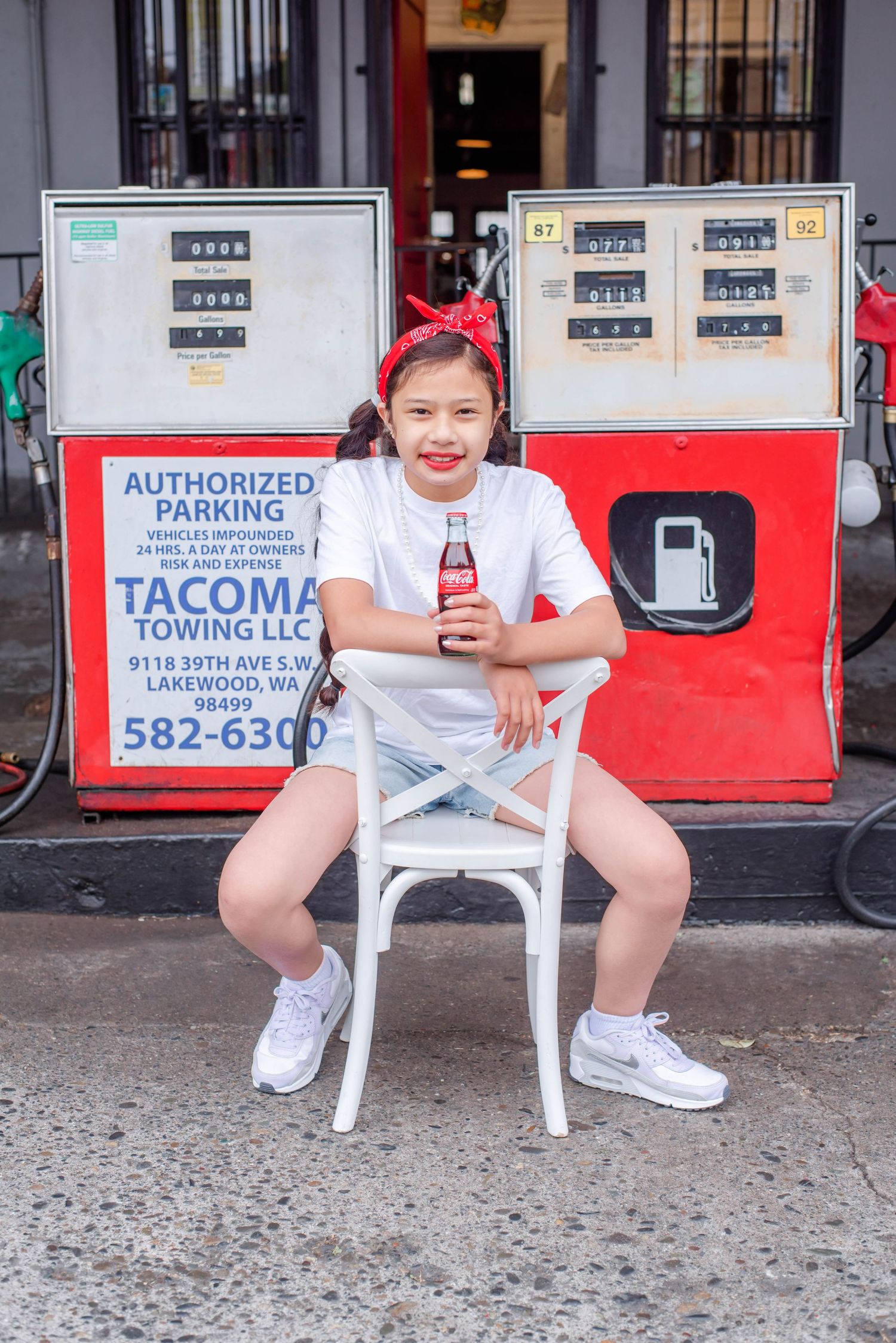 Person enjoying a red beverage while sitting on a white chair outside a storefront.