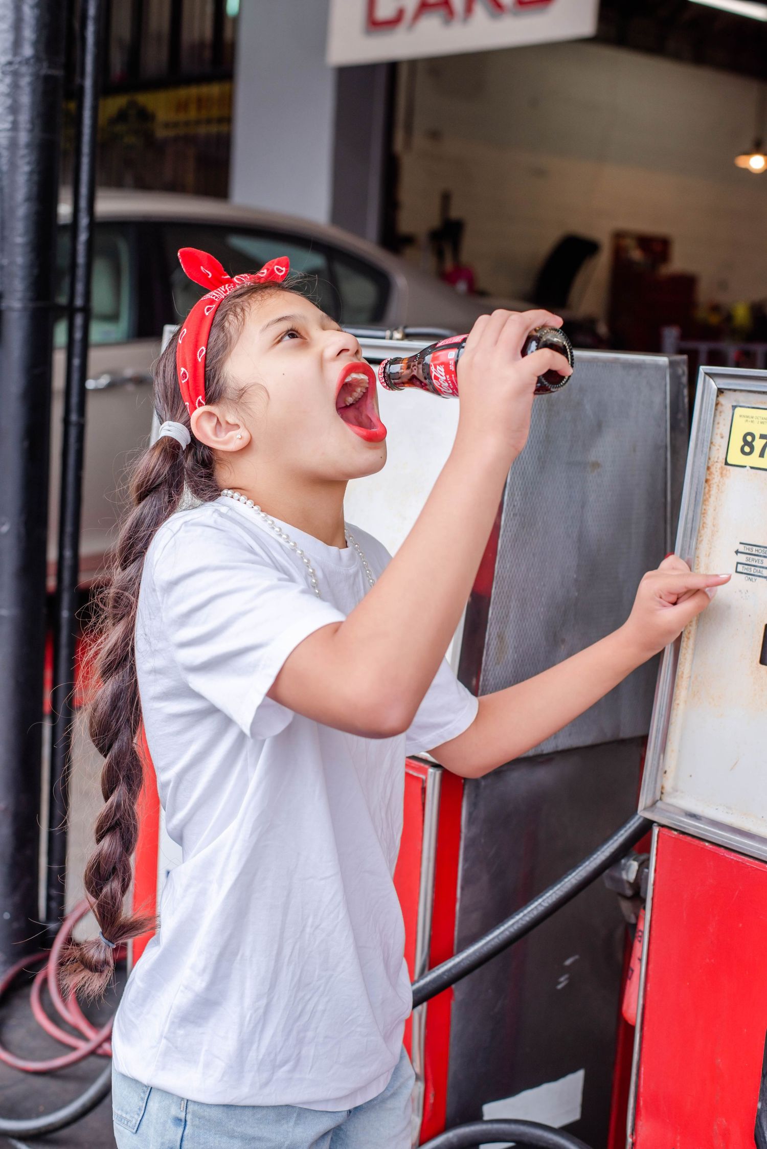Someone taking a drink from a bottle near vintage gas pumps and business signs.