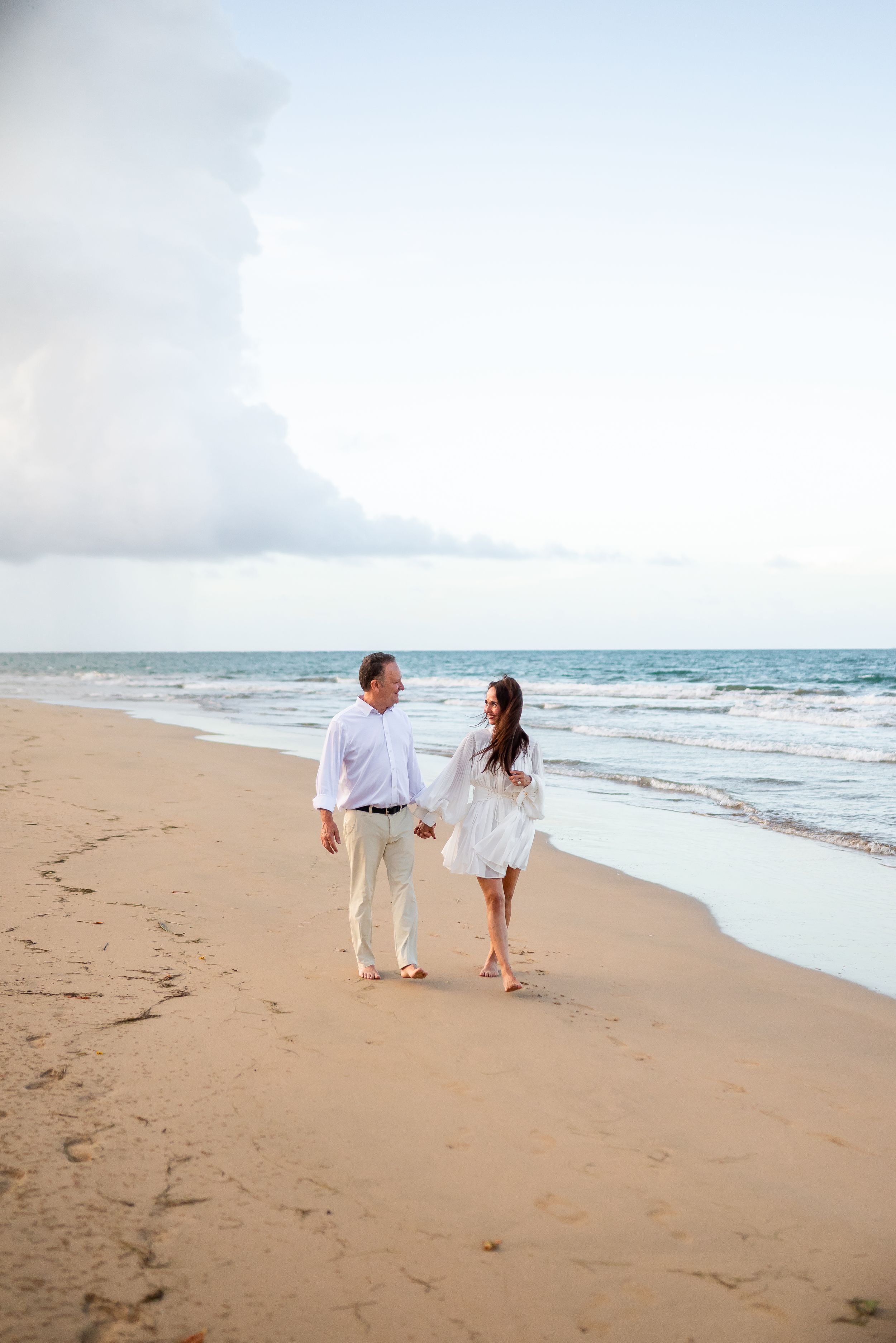 A couple takes a romantic stroll along the shoreline at sunset.