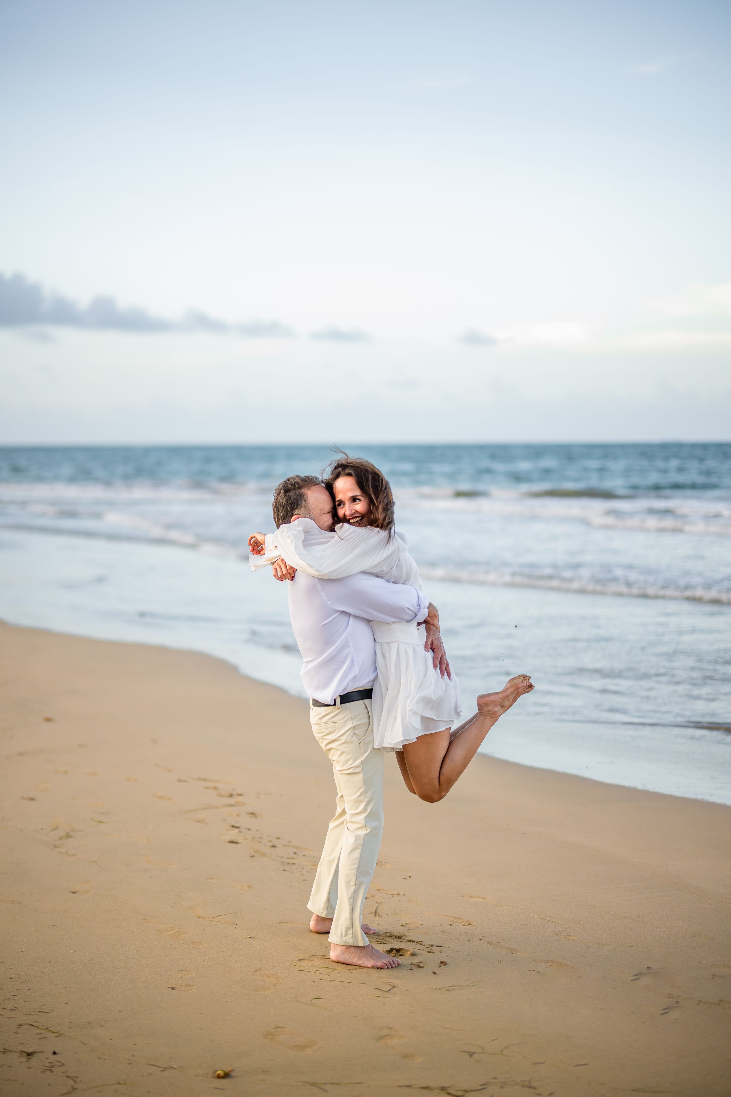 A joyful embrace on the beach with ocean waves in the background.
