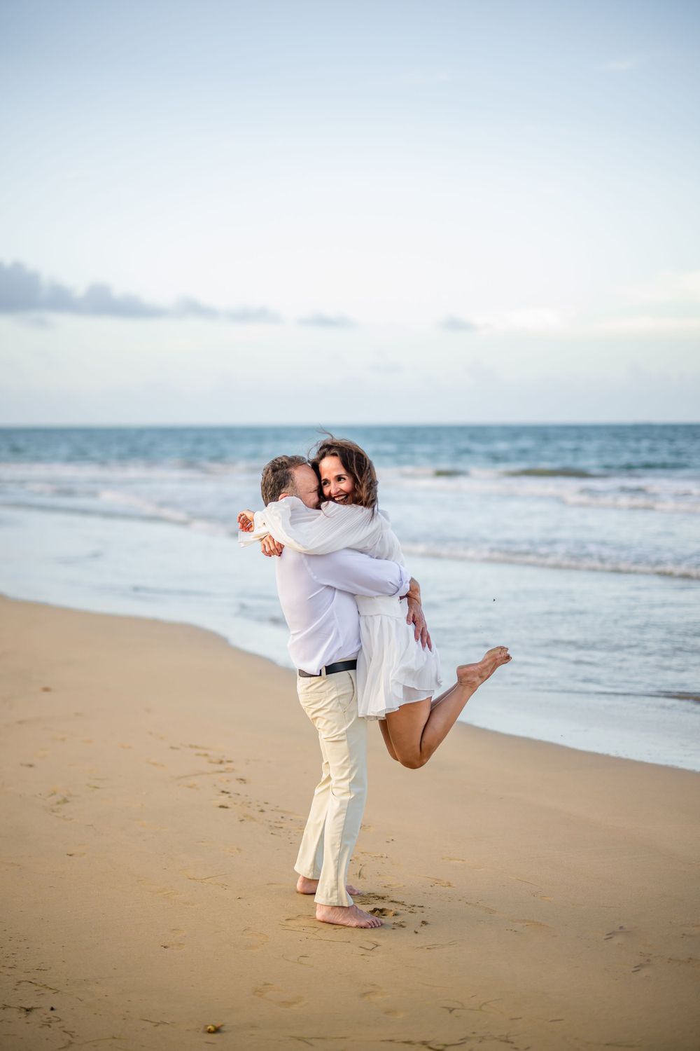 A joyful embrace on the beach with ocean waves in the background.