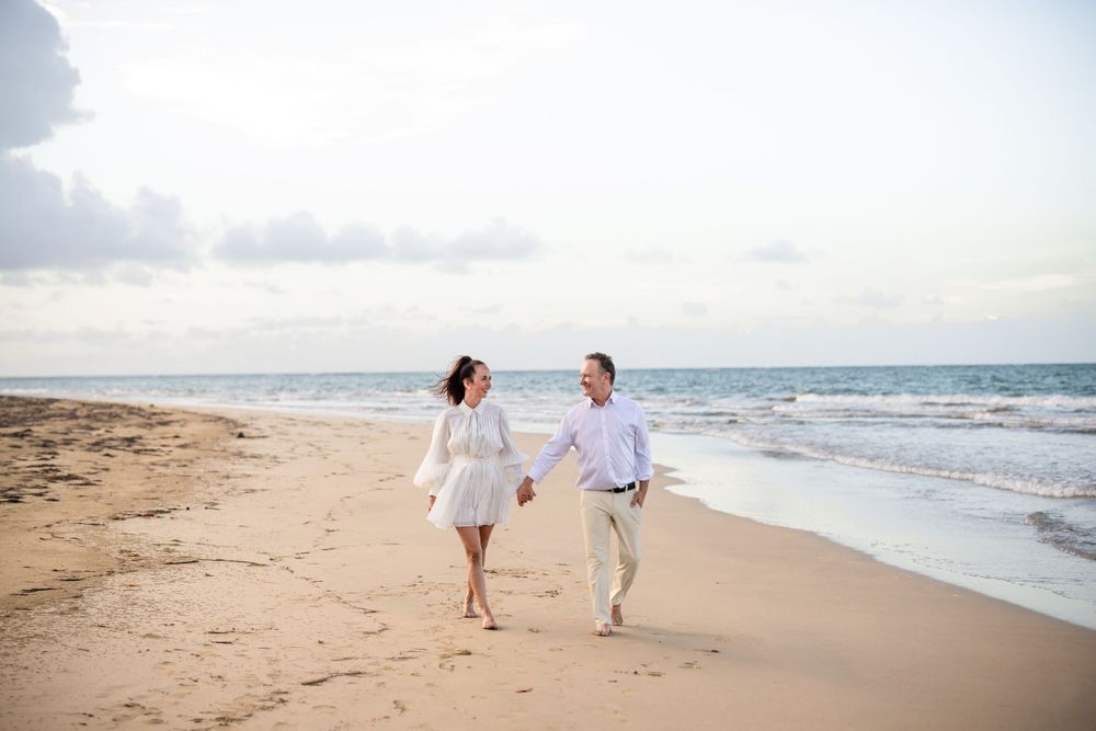 A couple walking hand in hand along a sandy beach at sunset.