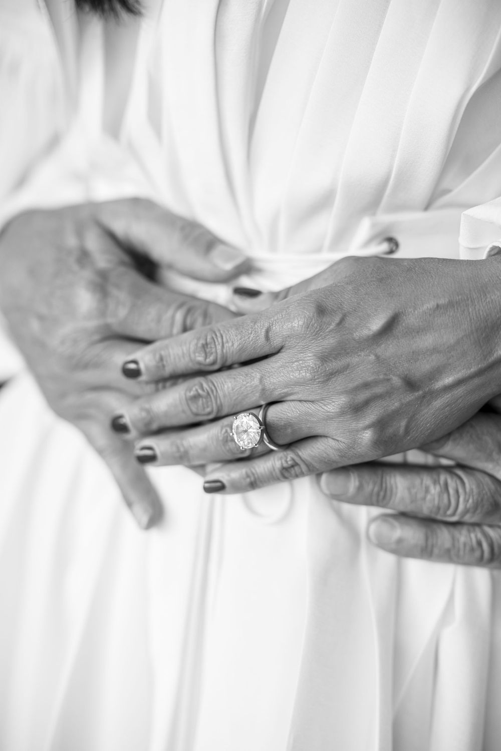 Close-up of hands showing off an engagement ring against a white dress.
