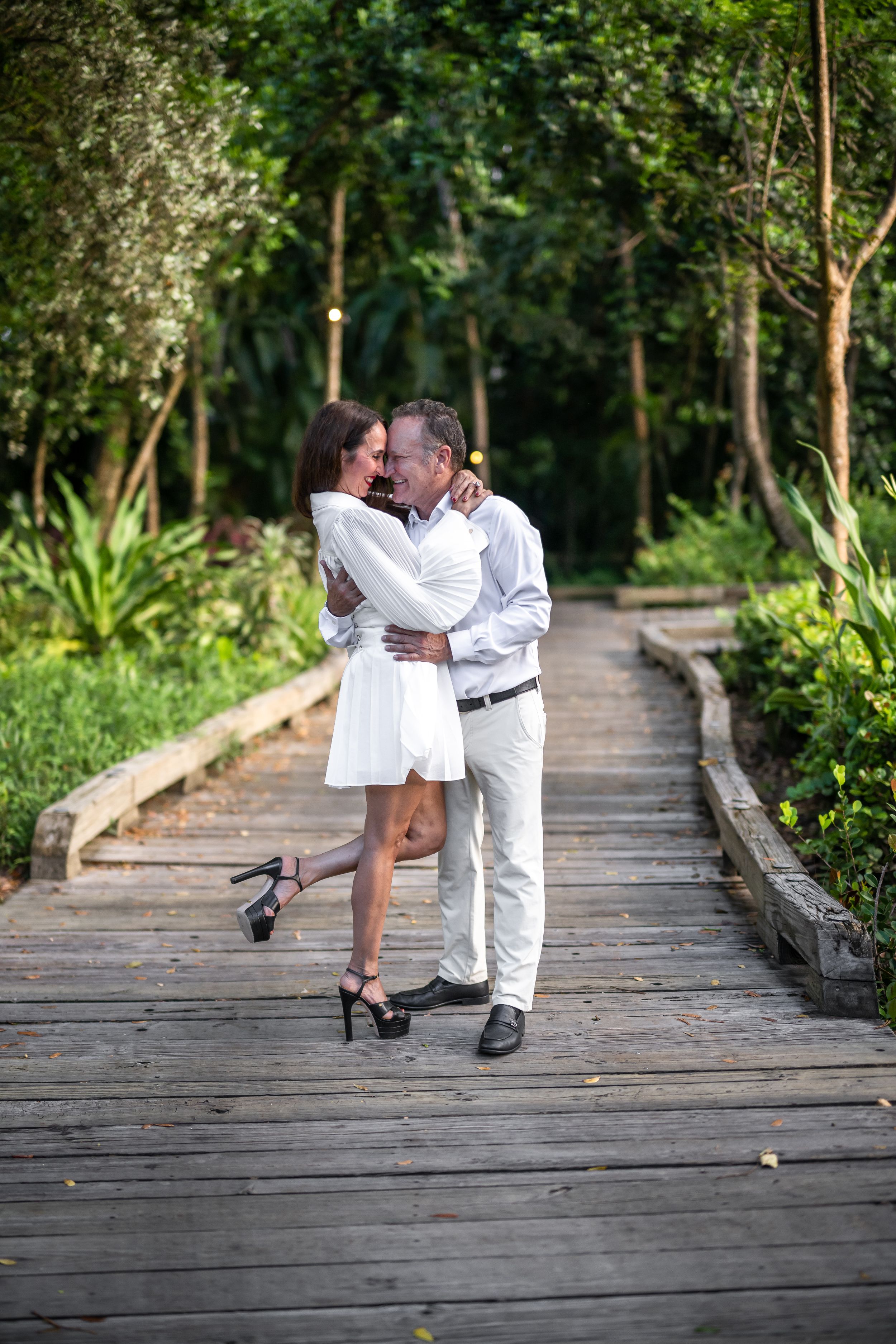 A couple shares an intimate moment on a wooden walkway surrounded by greenery.