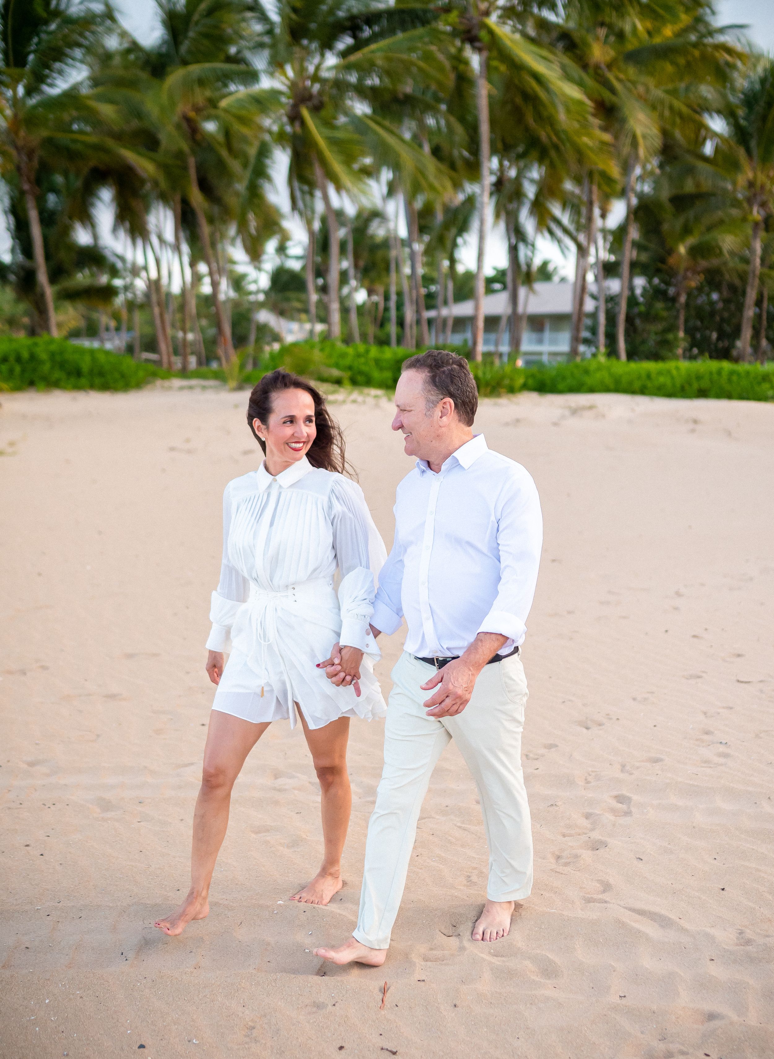 A couple walking barefoot together on a tropical beach with palm trees.