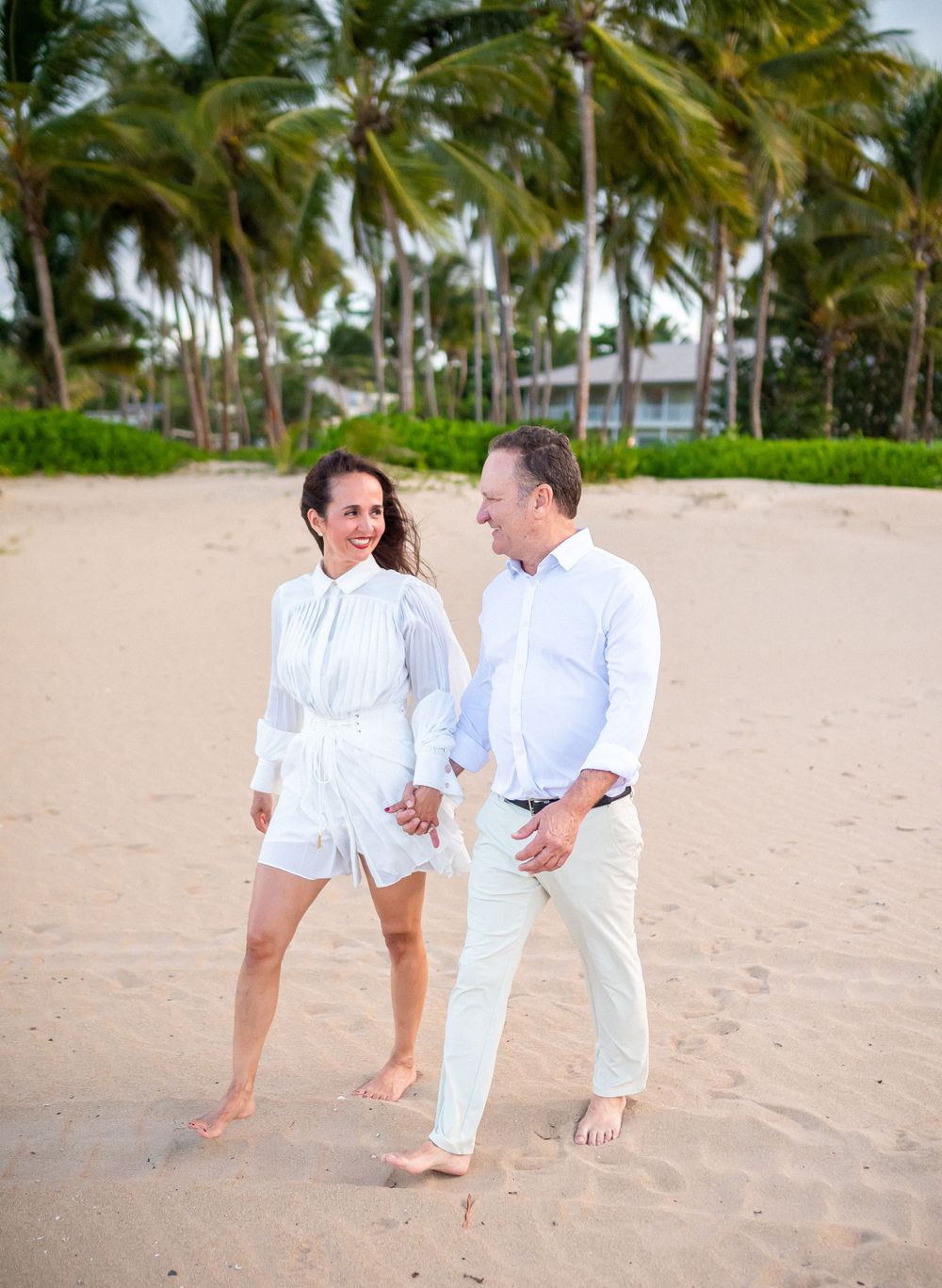 A couple walking barefoot together on a tropical beach with palm trees.