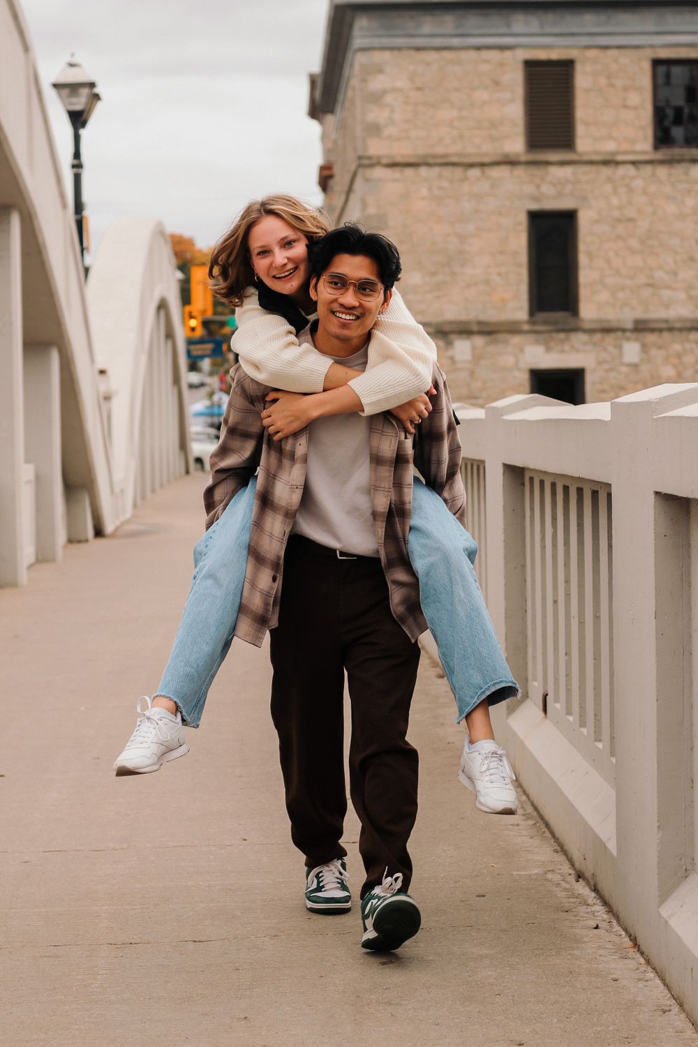 Couples photography of a man giving a woman a piggy-back ride and walking across a bridge.