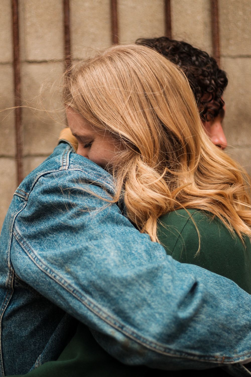 Couples photography from the side of a man in a denim jacket  hugging a woman in a green hoodie.