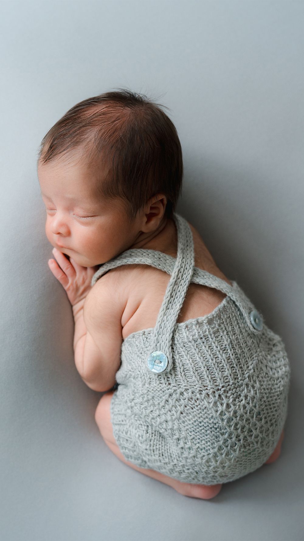 Sleeping newborn in soft gray knitted romper photographed from different angles against neutral background.
