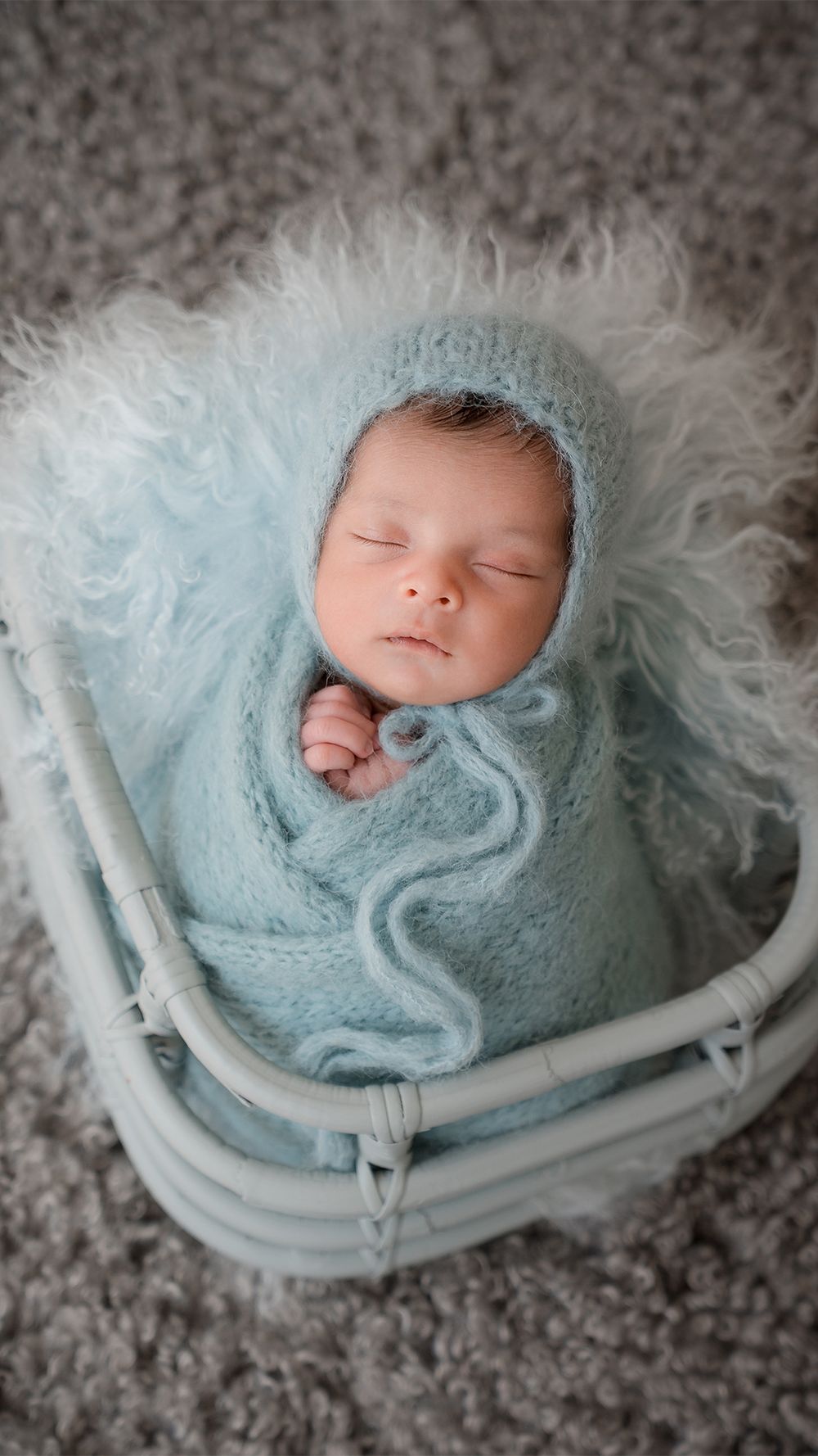 A sleeping newborn wrapped in soft blue blankets nestled in a white basket with fluffy white fur lining captured in Orangeville Ontario