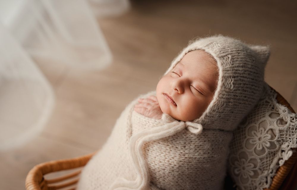 A sleeping newborn baby wrapped in soft knit blankets lies peacefully in a cozy brown setting.