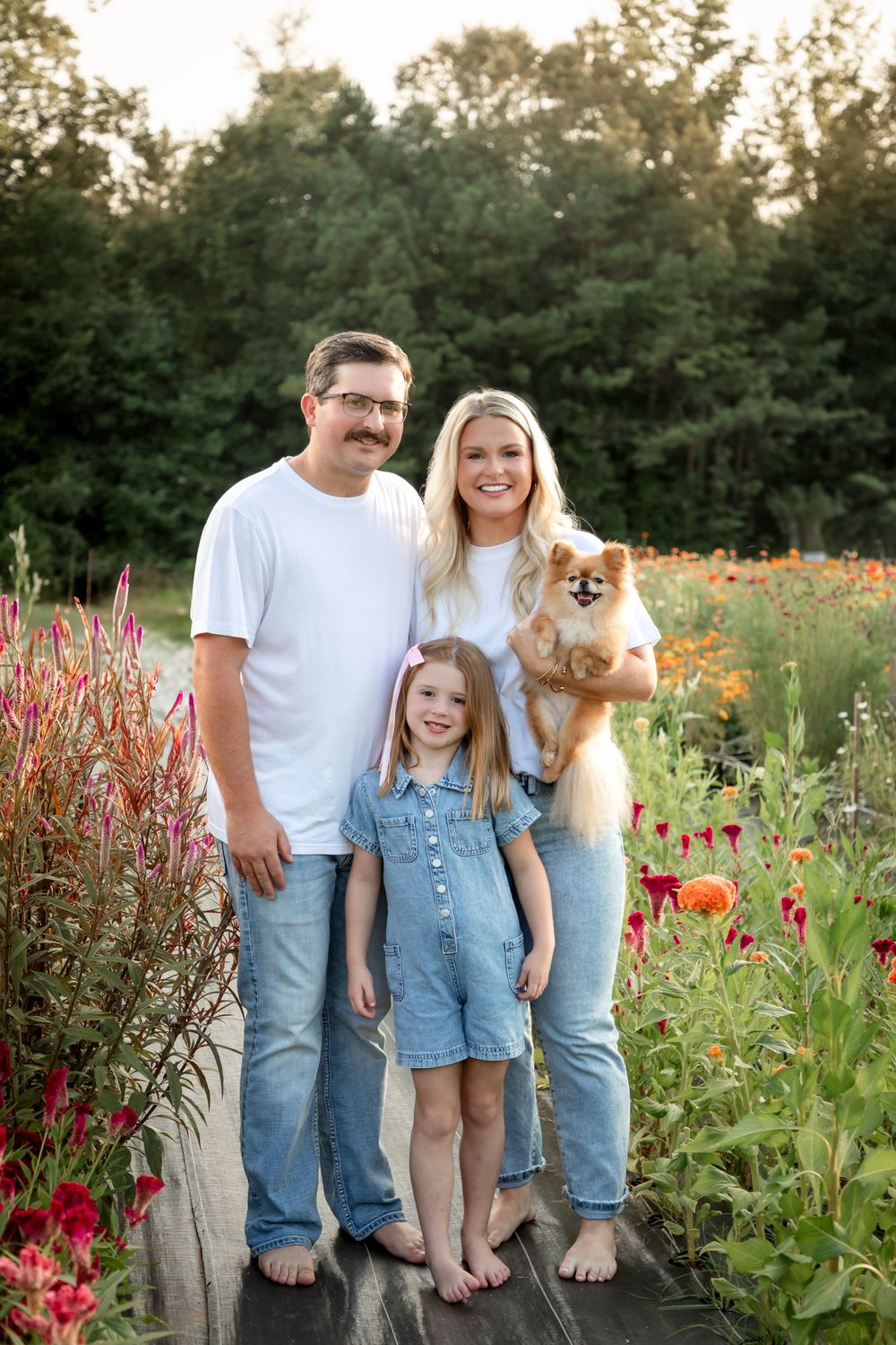 Family poses with their Pomeranian dog in a colorful flower garden.