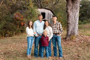 Family group poses outdoors in coordinated casual outfits against autumn foliage background.