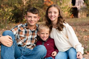 A family wearing casual fall clothing sits together on fallen leaves during an autumn outdoor photo session.