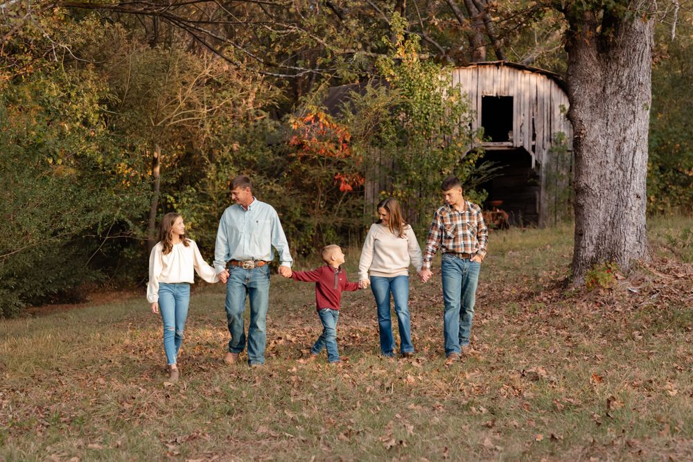 A group walks together on fallen autumn leaves with a rustic barn in the background.