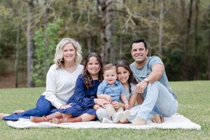 Family relaxes together on white blanket during outdoor photo session.