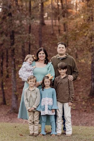 Family of six poses together against a backdrop of autumn trees.