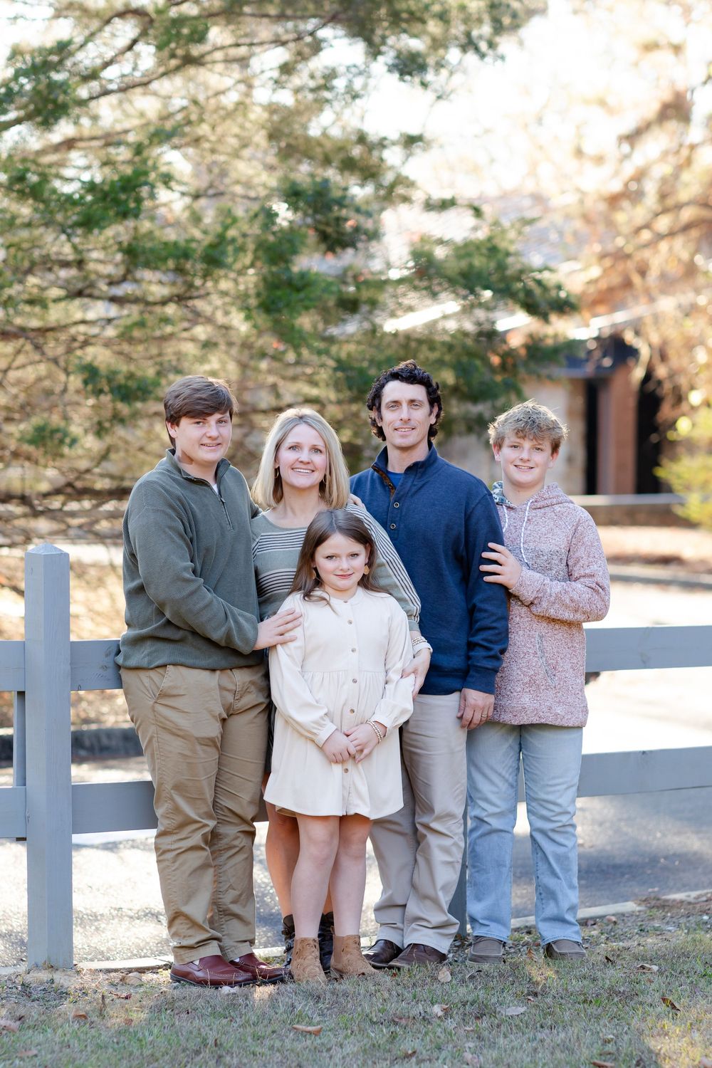 Family of five poses together by a white fence on an autumn day.