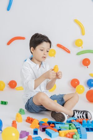 Child playing with colorful plastic building blocks and toys against white background.