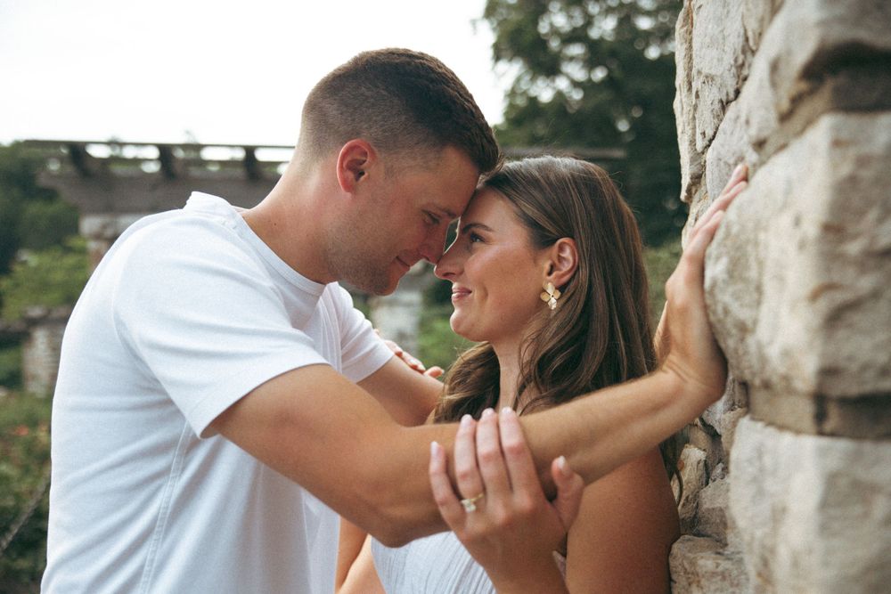 An intimate moment captured between a couple against a stone wall backdrop in a garden.