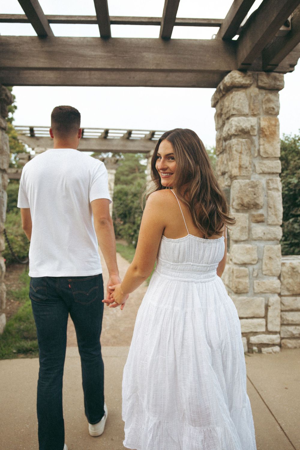 A candid shot of a couple walking hand in hand under a wooden pergola structure.