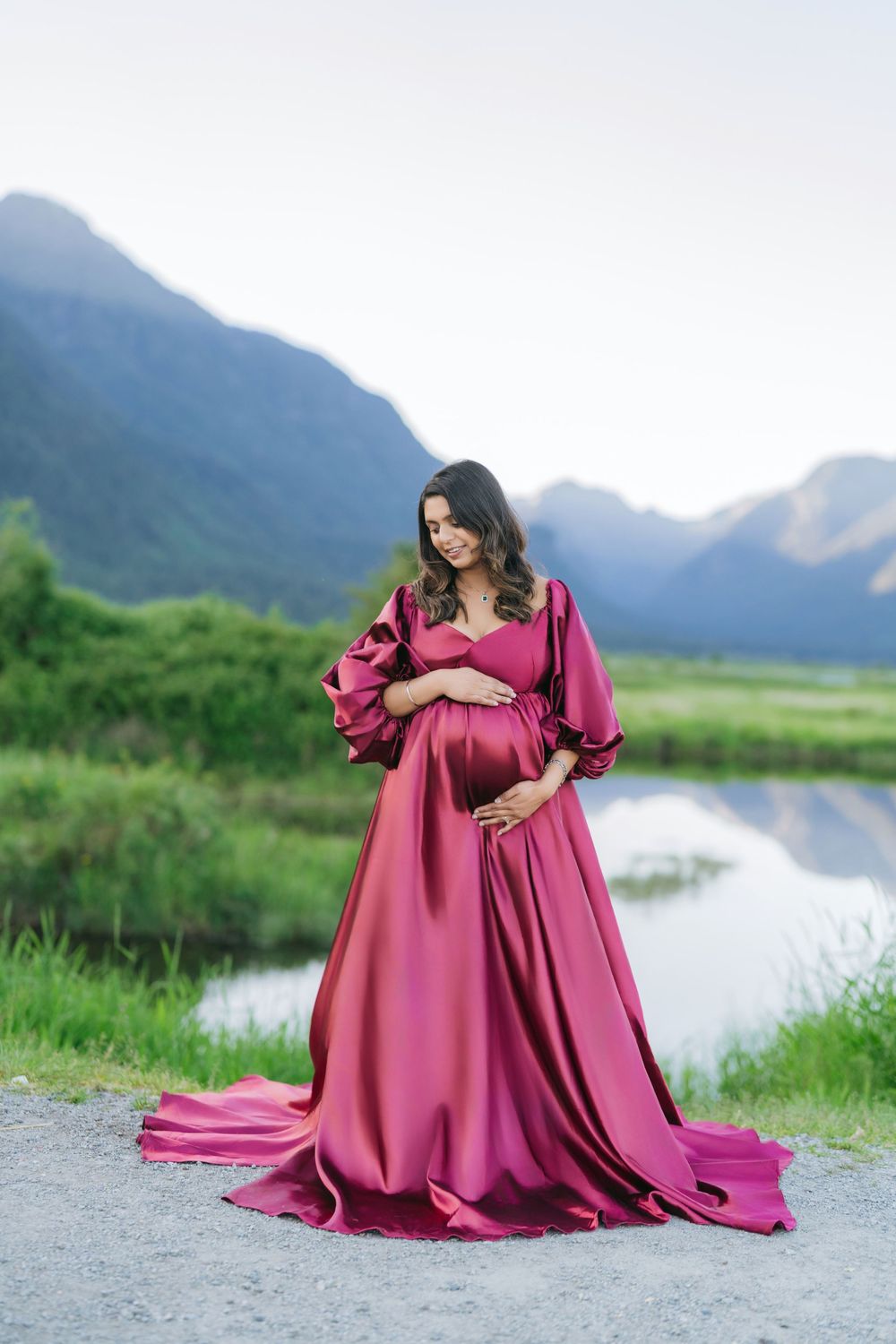 Two matching burgundy gowns photographed in a serene mountain lakeside setting.