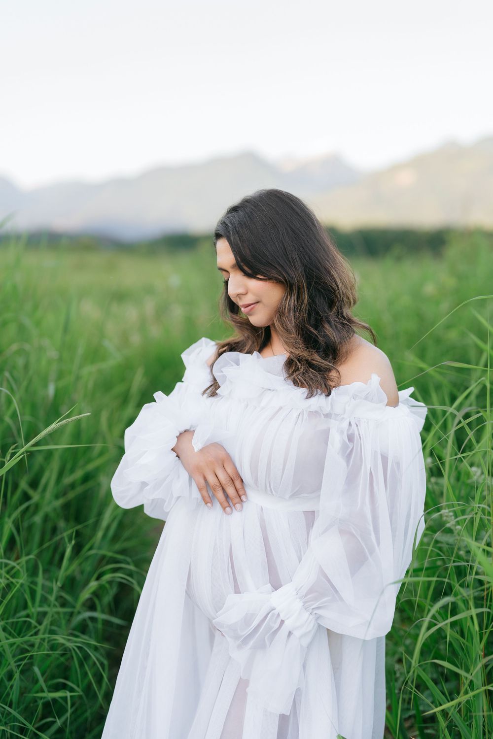 An ethereal white dress photographed in a grassy field with mountains in the background.
