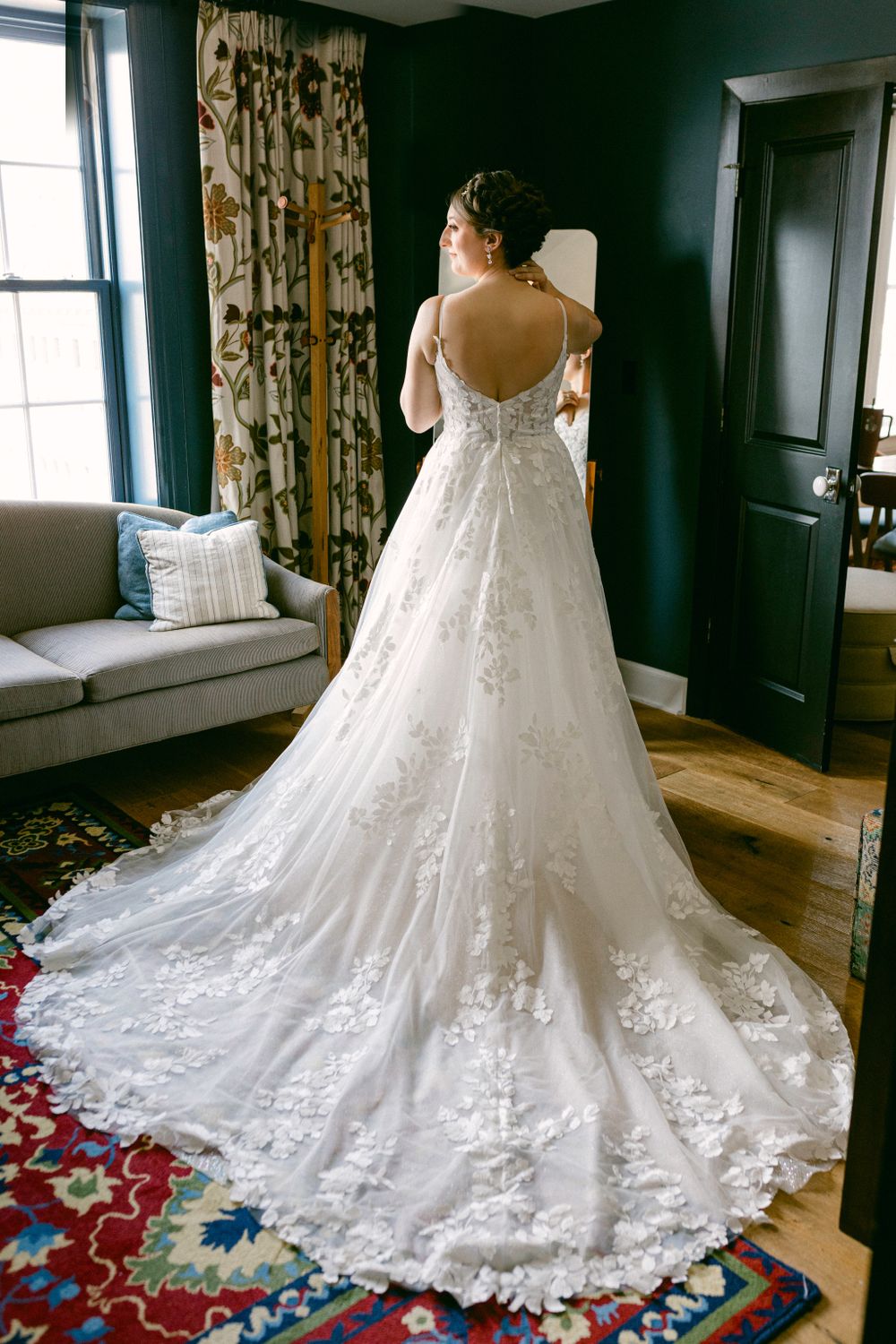 Elegant lace wedding dress with long train displayed in a sunlit room with dark walls.