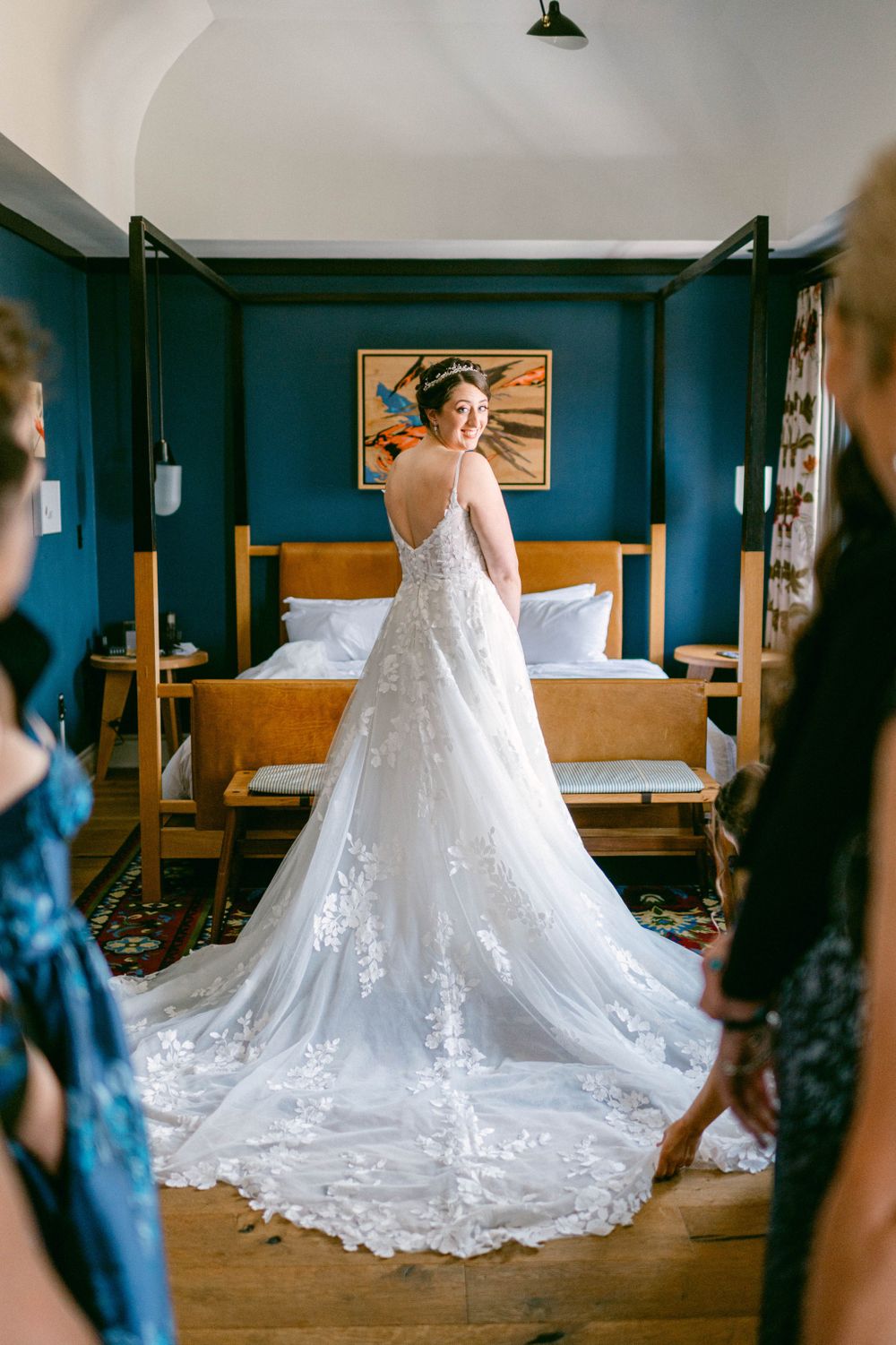 Wedding dress with intricate lace train displayed in a room with navy blue walls.