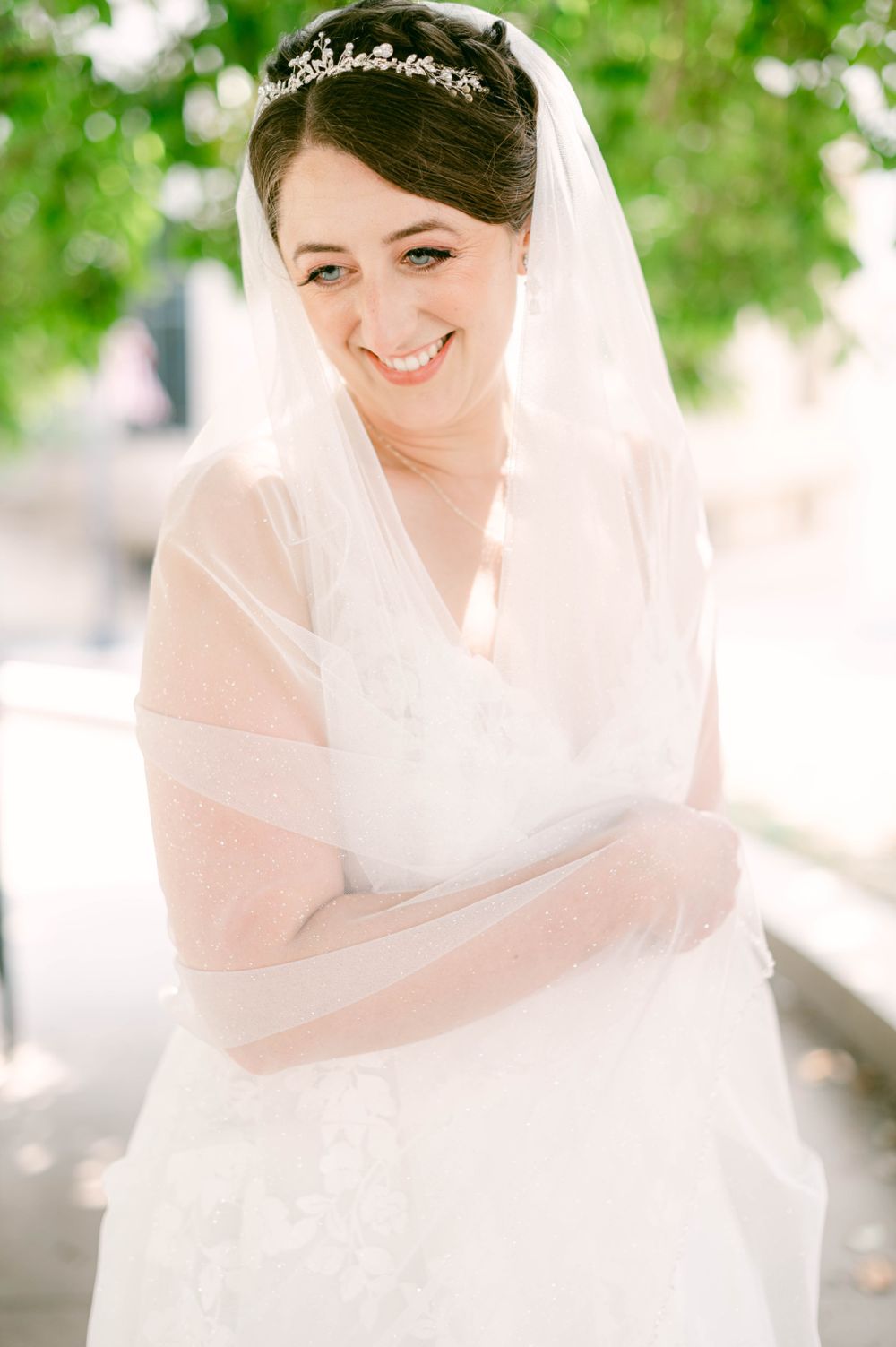 Close-up portrait of bride wearing veil and tiara against bright outdoor setting.