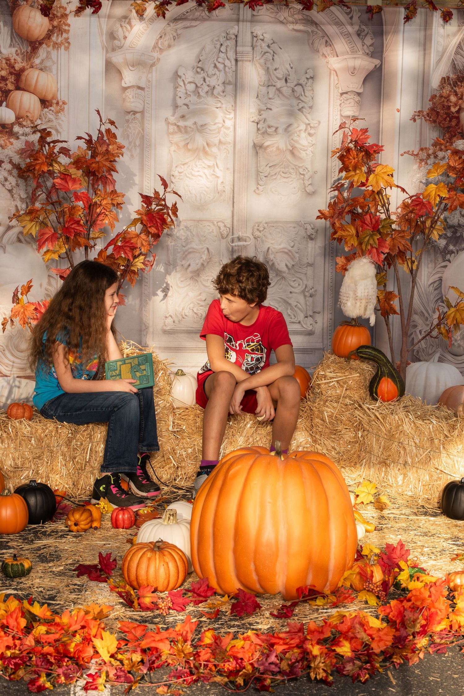 An autumn themed photo setting with pumpkins, hay bales, and orange fall foliage against a white backdrop.